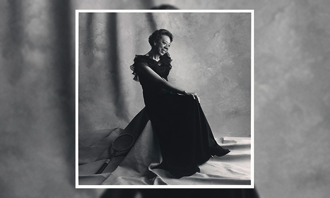 Image of Althea Gibson in a black, full length gown seated in front of a photography studio backdrop.