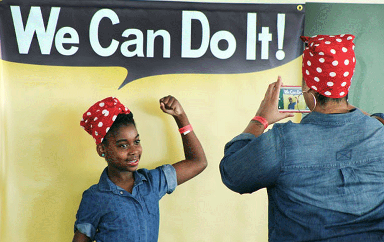 Girl takes photo in front of the “We Can Do It” sign at Rosie the Riveter/WWII Home Front National Historical Park